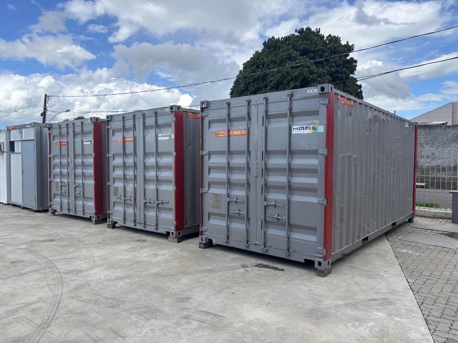 Três containers marítimos de 20 pés cinza com cantos vermelhos no pátio da Haas